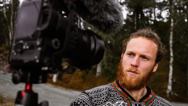A bearded man records a video outdoors using a professional camera, showcasing selective focus and vlogging setup. Comparing the main travel creator campaign business models for England operators